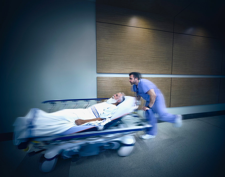 Motion blurred image of a hospital worker rushing a patient on a gurney down a hallway